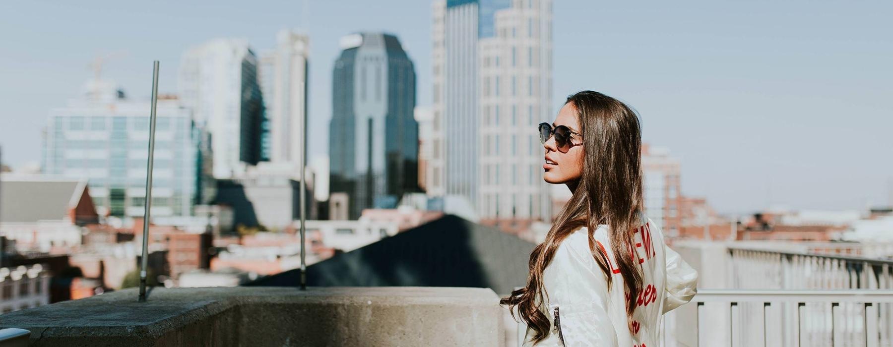 woman with sunglasses stands on a rooftop overlooking the city
